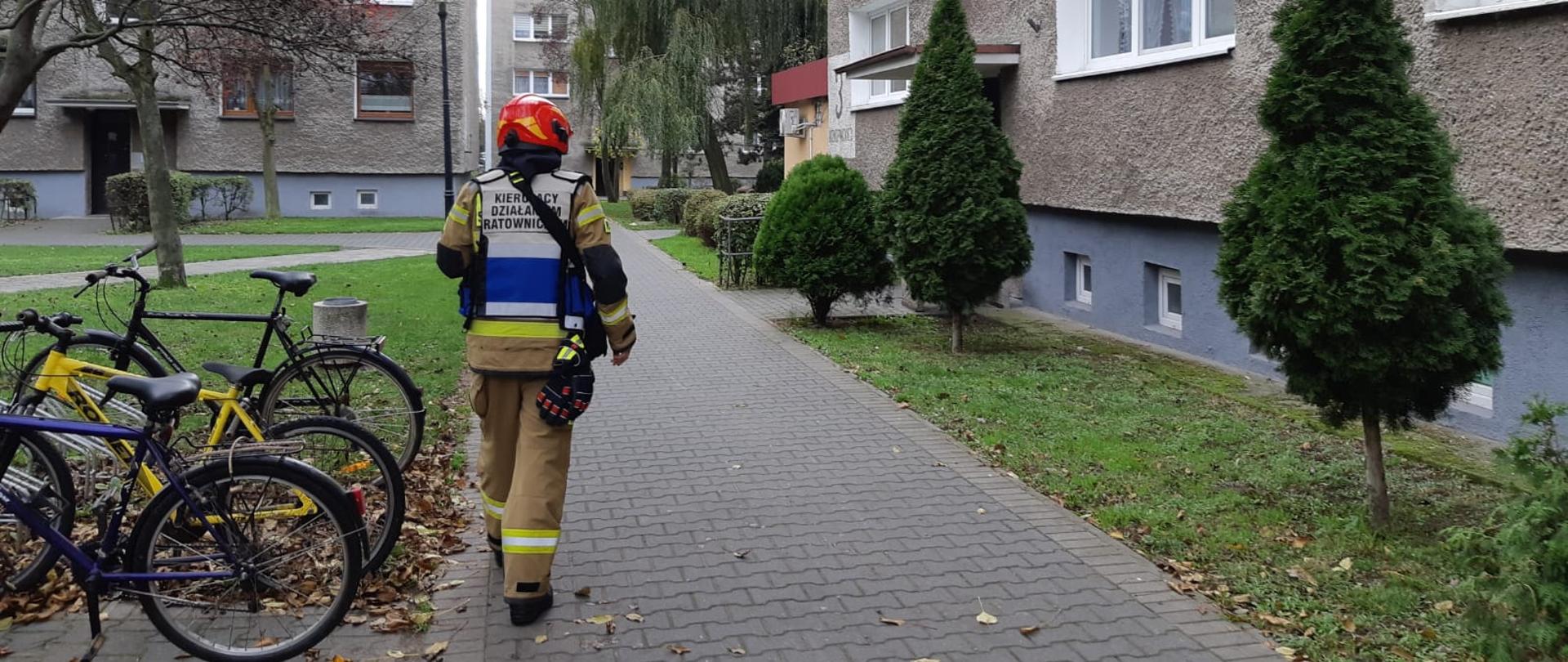 Zdjęcie przedstawia kierującego działaniem ratowniczym przy bloku wielorodzinnym.