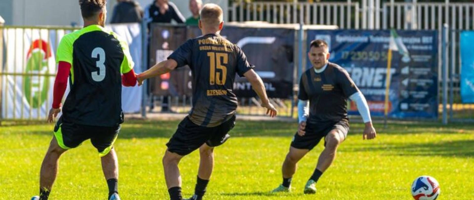 Zdjęcie przedstawia trzech mężczyzn grających w piłkę nożną