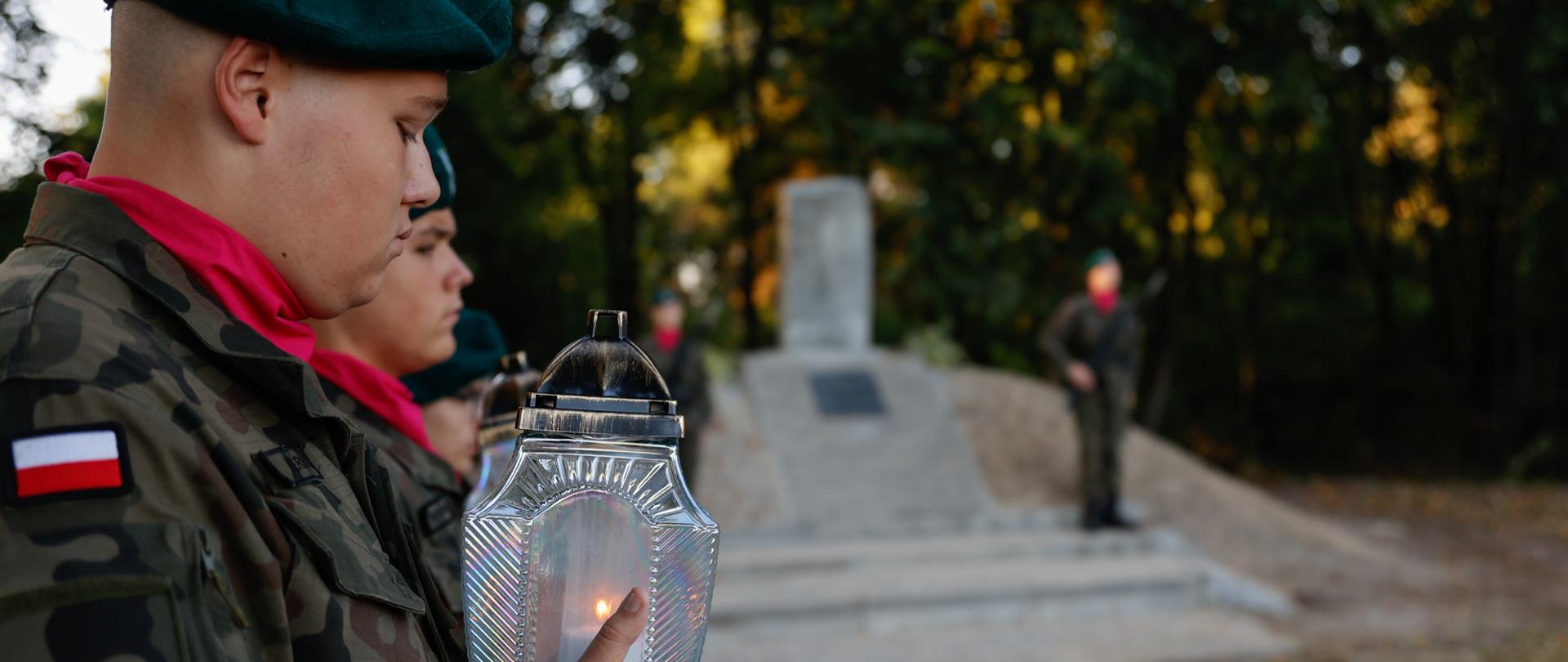 Chłopcy w mundurach trzymają znicze zapalone w dłoniach.