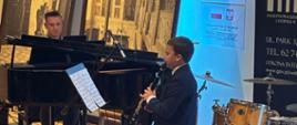 Zdjęcie przedstawia ucznia grającego na klarnecie z towarzyszeniem akompaniatora przy fortepianie podczas koncertu w holu Pałacu Radolińskich.