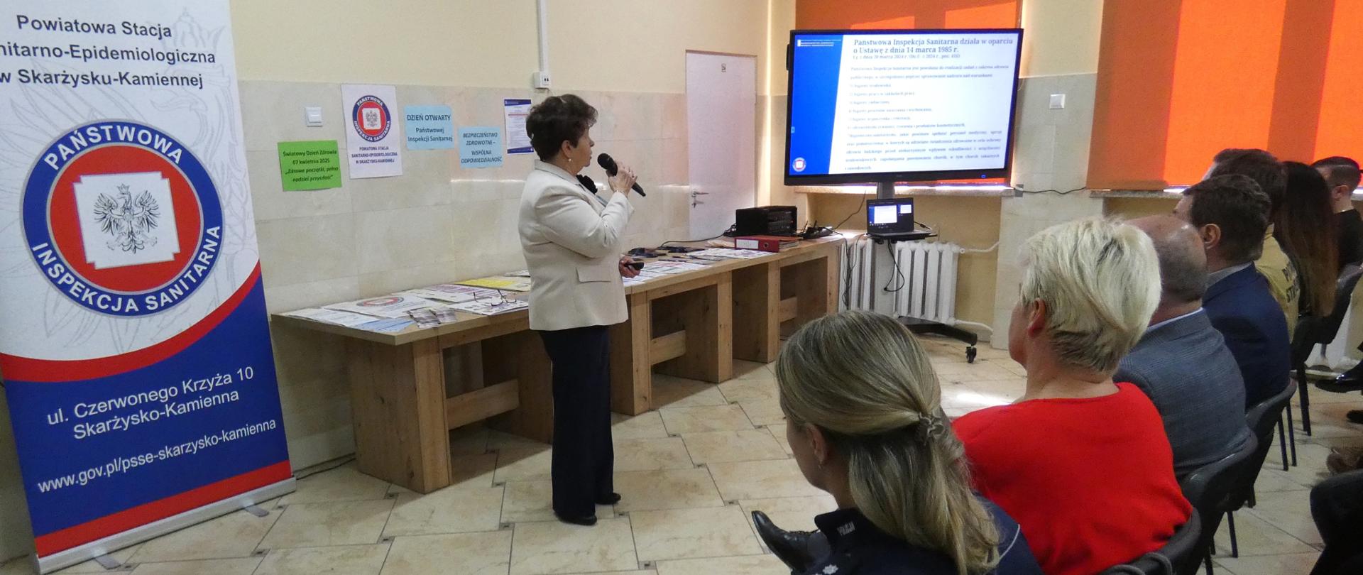 Widok prowadzącego z uczestnikami Dnia Otwartego Państwowej Inspekcji Sanitarnej w tle.