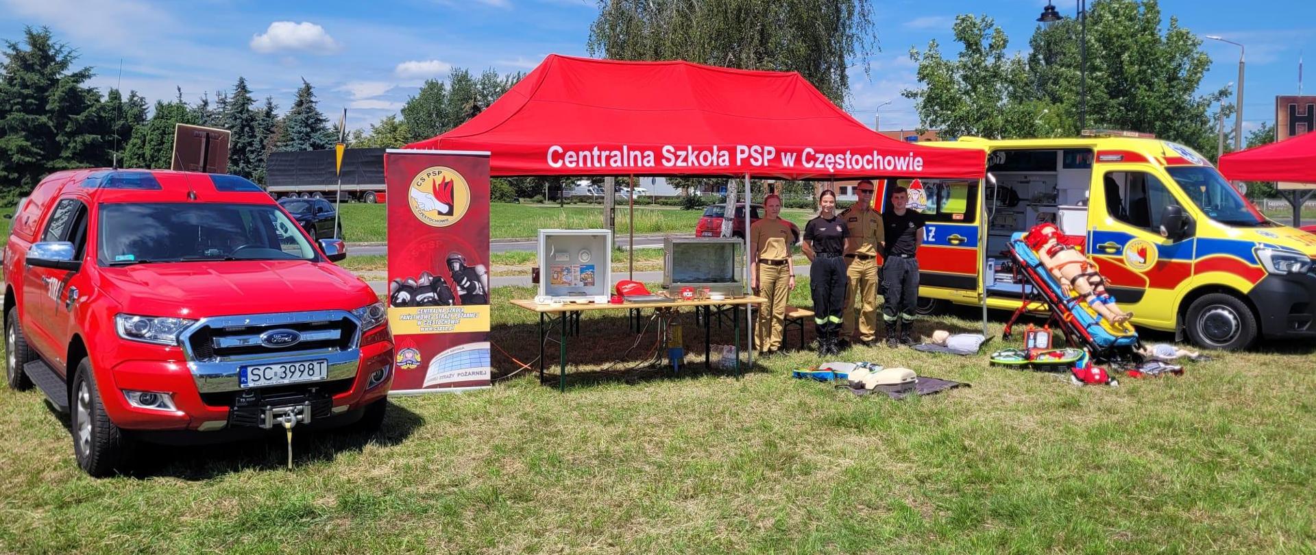 Od lewej samochód służbowy typu Ford Ranger następnie czworo strażaków Centralnej Szkoły PSP stojących przy stoisku CS PSP oraz samochód typu karetka