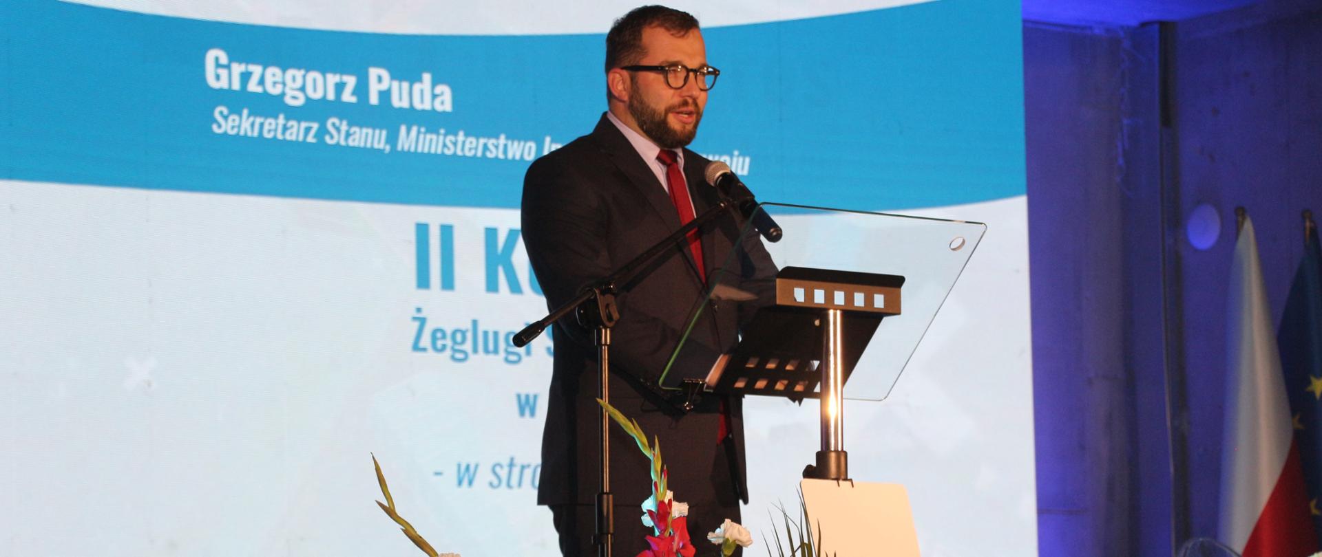 wiceminister Grzegorz Puda stoi przy pulpicie i mówi do mikrofonu, za nim napis II Kongres Żeglugi Śródlądowej
