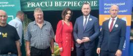 Kobieta i czterech mężczyzn pozują do zdjęcia przed namiotem ze stoiskiem KRUS.