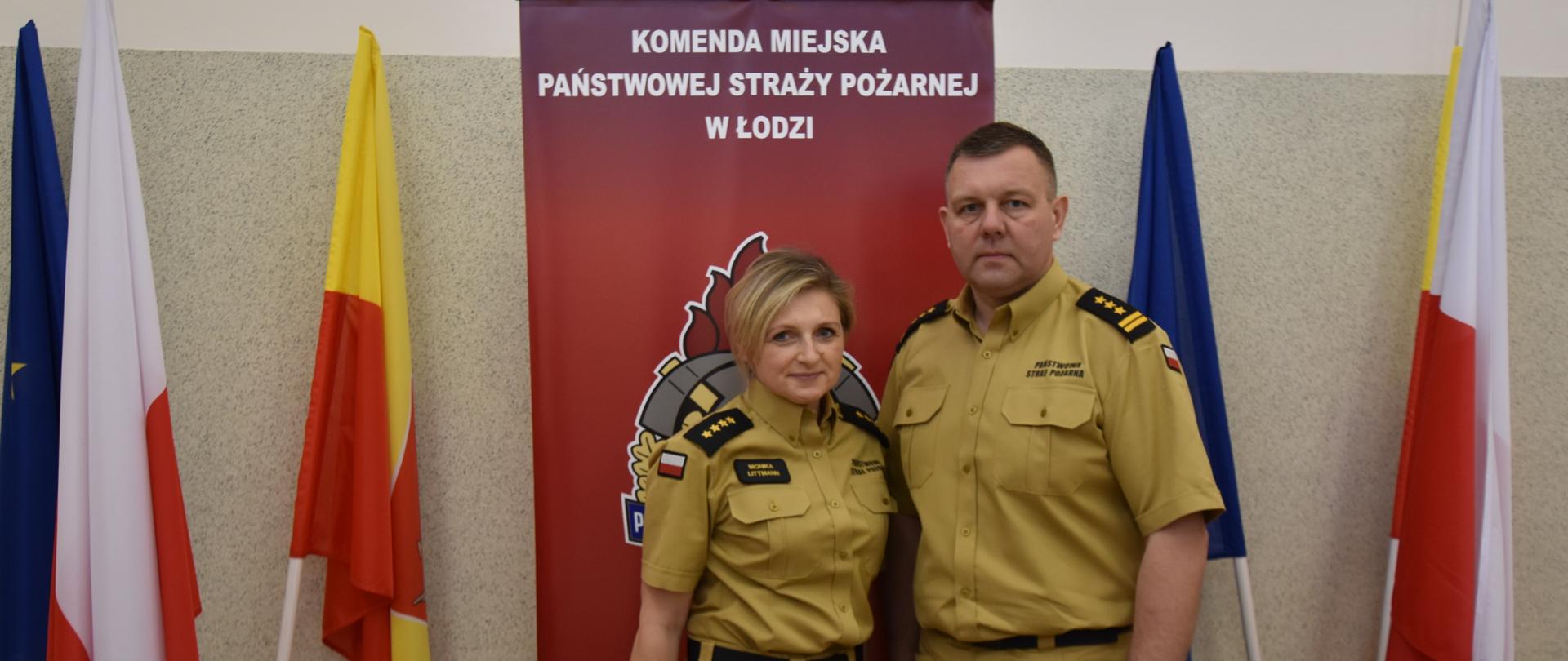 Strażacy PSP w nowym piaskowym umundurowaniu na tle logo PSP obok flagi RP, UE oraz Miasta Łodzi