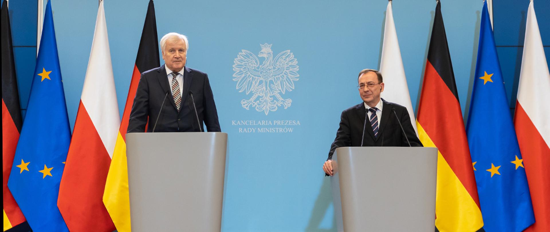 Na zdjęciu widać ministra Mariusza Kamińskiego i Horsta Seehofernera szefa niemieckiego MSW stojących za mównicami w trakcie konferencji prasowej, w tle widać flagi Niemiec, Polski i UE.