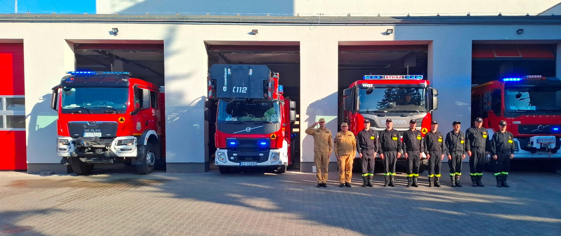 Strażacy na tle samochodów strażackich oddają hołd