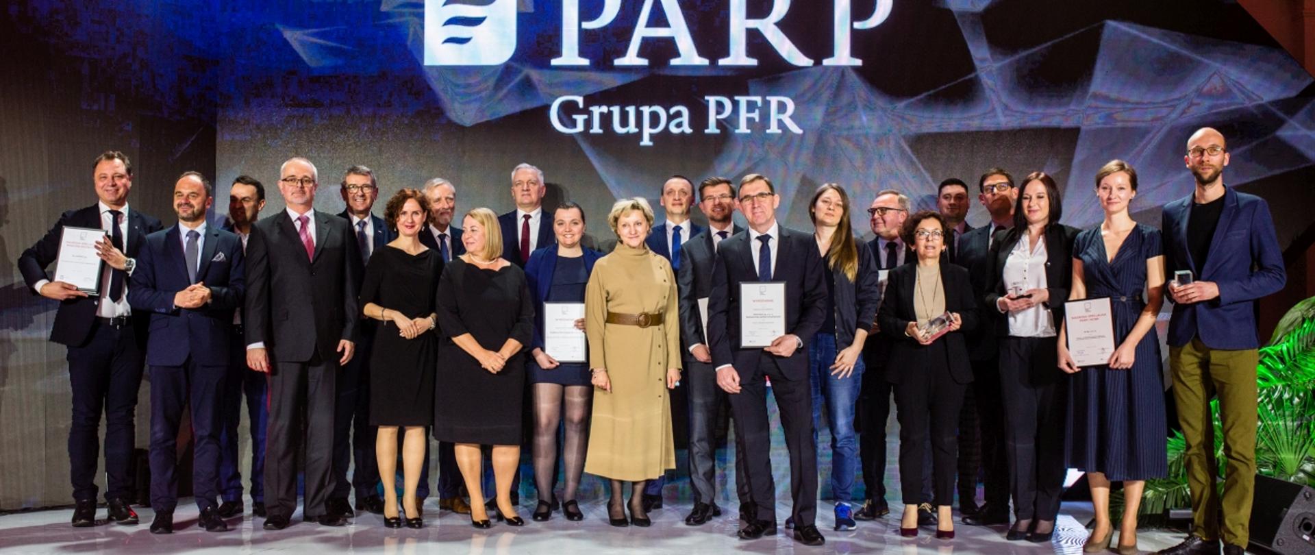 Zdjęcie zbiorowe, laureaci konkursu stoją na tle ściany z napisem PARP.