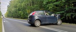 Zdjęcie przedstawia rozbity samochód osobowy marki Fiat Grande Punto znajdujący się na środku drogi. 