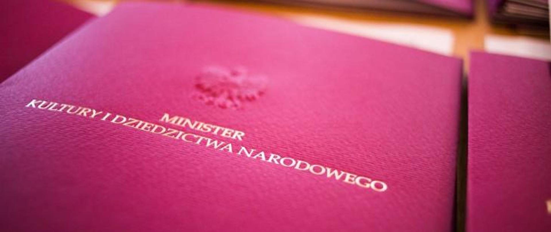 zdjęcie przedstawia bordowa okłakę z wyłoczonym wizerunkiem orła i złotym napisem Minister Kultury i Dziedzictwa Narodowego