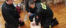 Na zdjęciu widać trzech druhów OSP w trakcie egzaminu teoretycznego. Druhowie udzielają resuscytacji krążeniowo-oddechowej na fantomie. Zdjęcie wykonane na świetlicy Komendy Powiatowej PSP w Oleśnie.