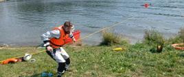Na zdjęciu widoczny ratownik stojący na brzegu wyciągający na linie ratownika wraz z poszkodowanym z wody.