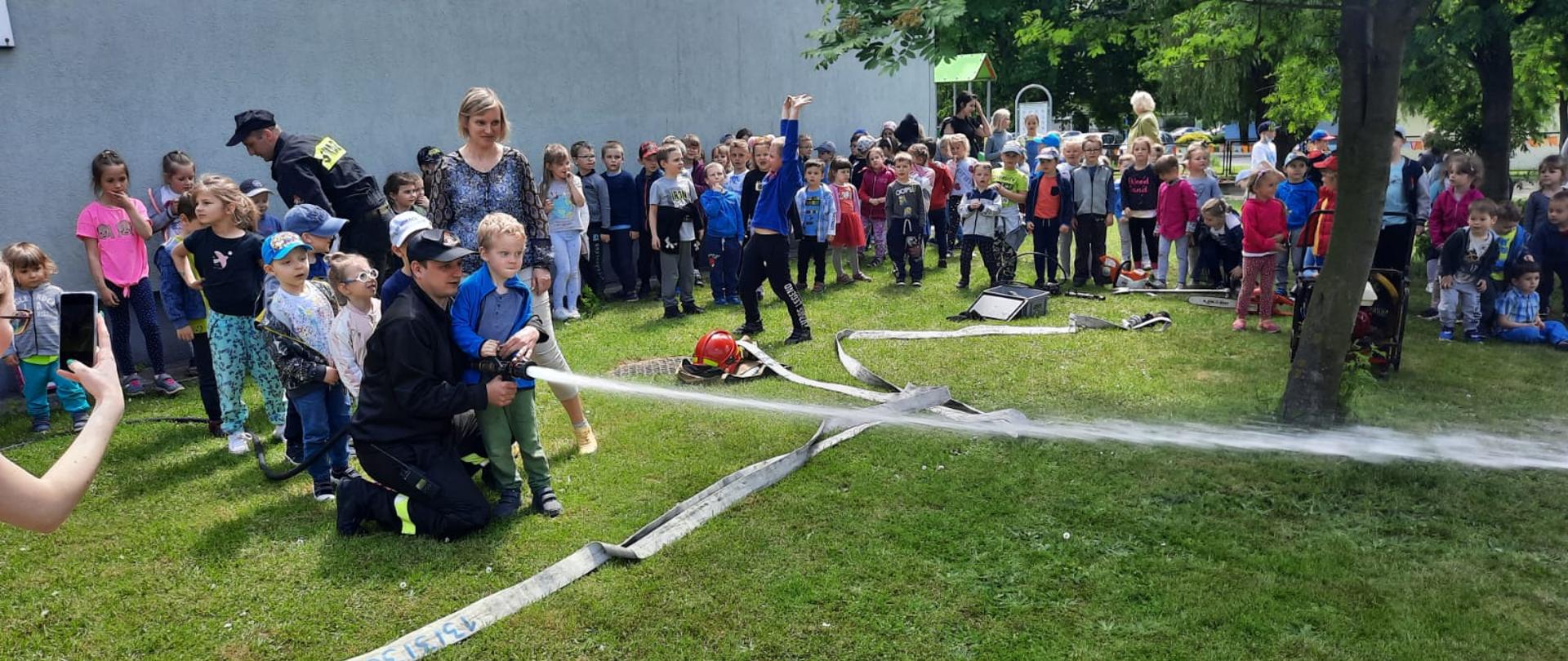 Zdjęcie przedstawia strażaka oraz dzieci z przedszkola podczas pokazów straży pożarnej.