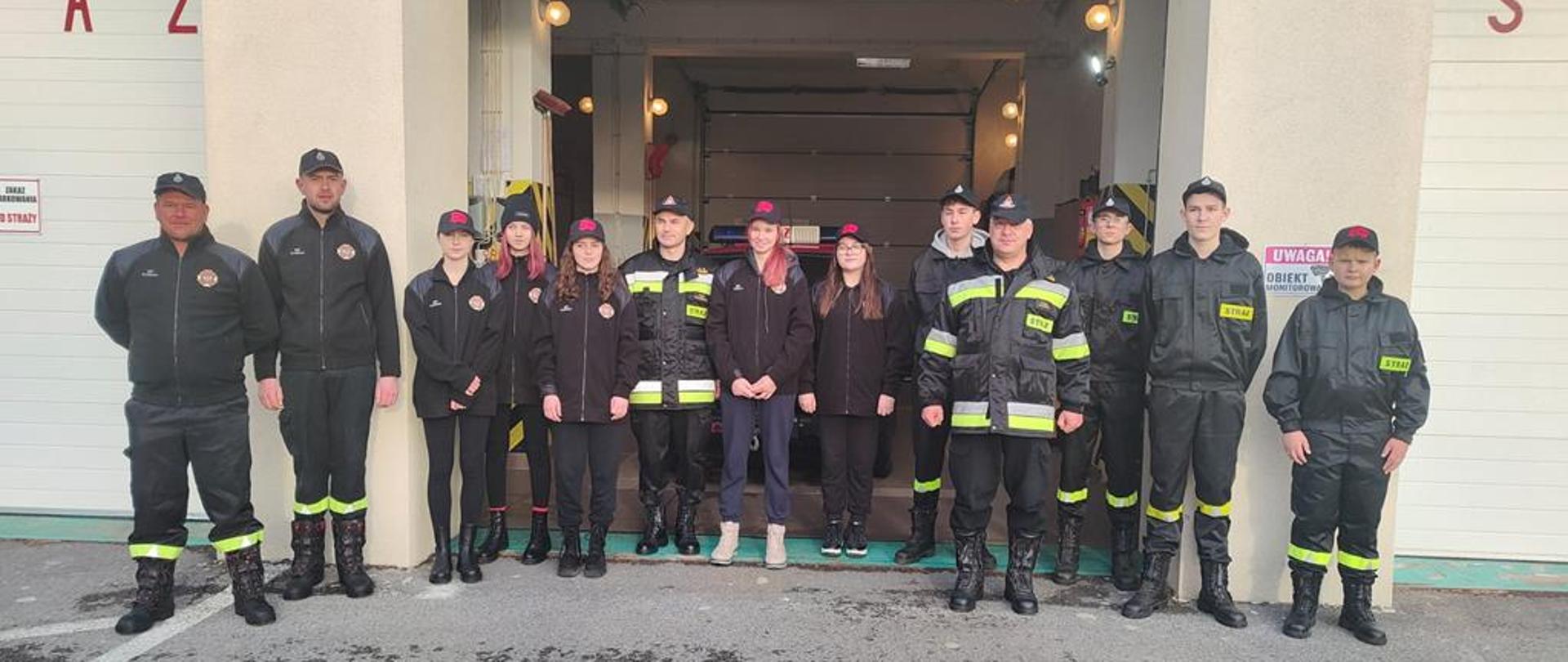 Przed garażem jednostki OSP stoją druhowie z komendantami.
