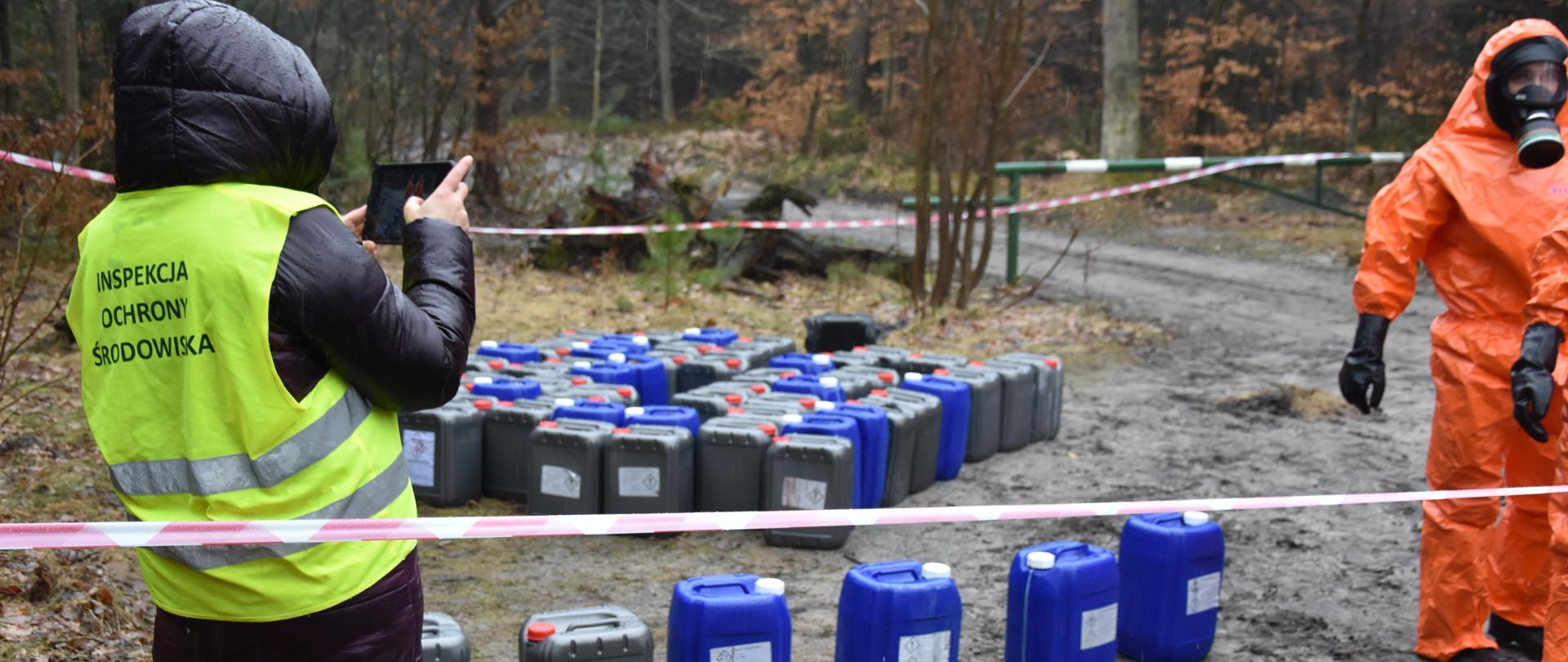 Inspektor Wojewódzkiego Inspektoratu Ochrony środowiska monitoruje pobór próbek z pojemników o pojemności 20 l porzuconych na ziemi.