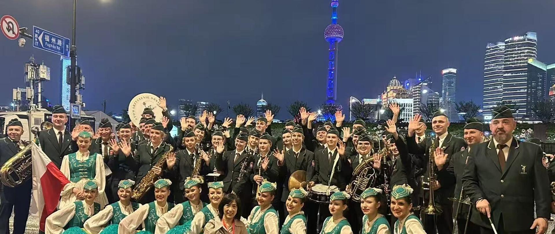 Grupa muzyków z orkiestry i tancerki na tle nocnego Szanghaju