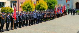 Na zdjęciu widoczna zbiórka w szeregu pododdziału OSP Frysztak oraz pocztów flagowych. W tle zabudowania rynku we Frysztaku.