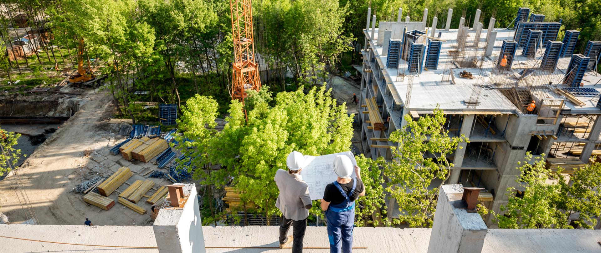Top view on the construction site of residential buildings on the green area with two workers looking on the construction process