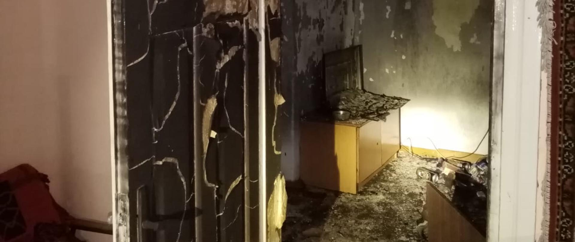 Budynek w którym miał miejsce pożar - wnętrze budynku. Widoczne okopcone drzwi oraz spalone wnętrze pokoju.
