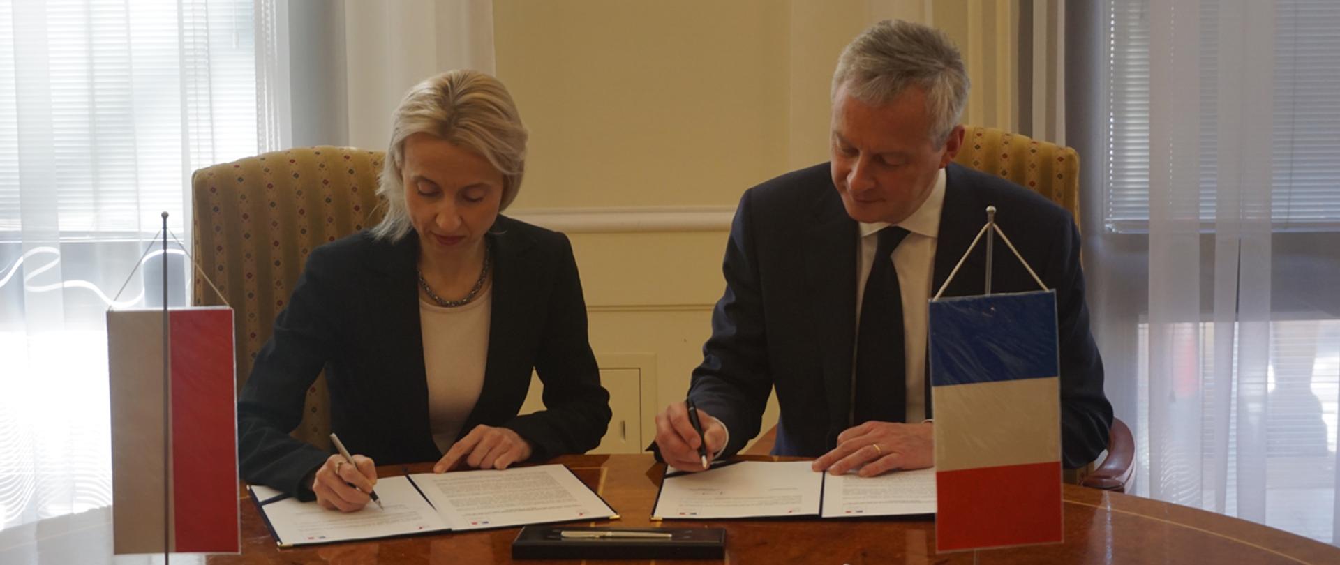 Minister finansów Teresa Czerwińska i minister gospodarki i finansów Bruno Le Maire podpisują deklarację o współpracy podatkowej przy flagach Polski i Francji