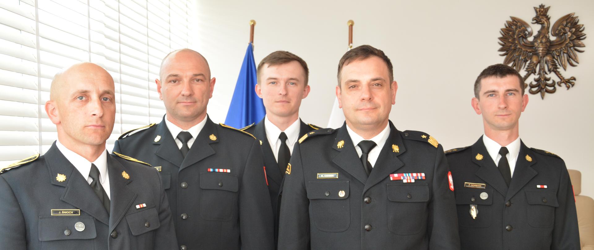 Czterech mężczyzn w mundurach strażackich pozuje do zdjęcia.