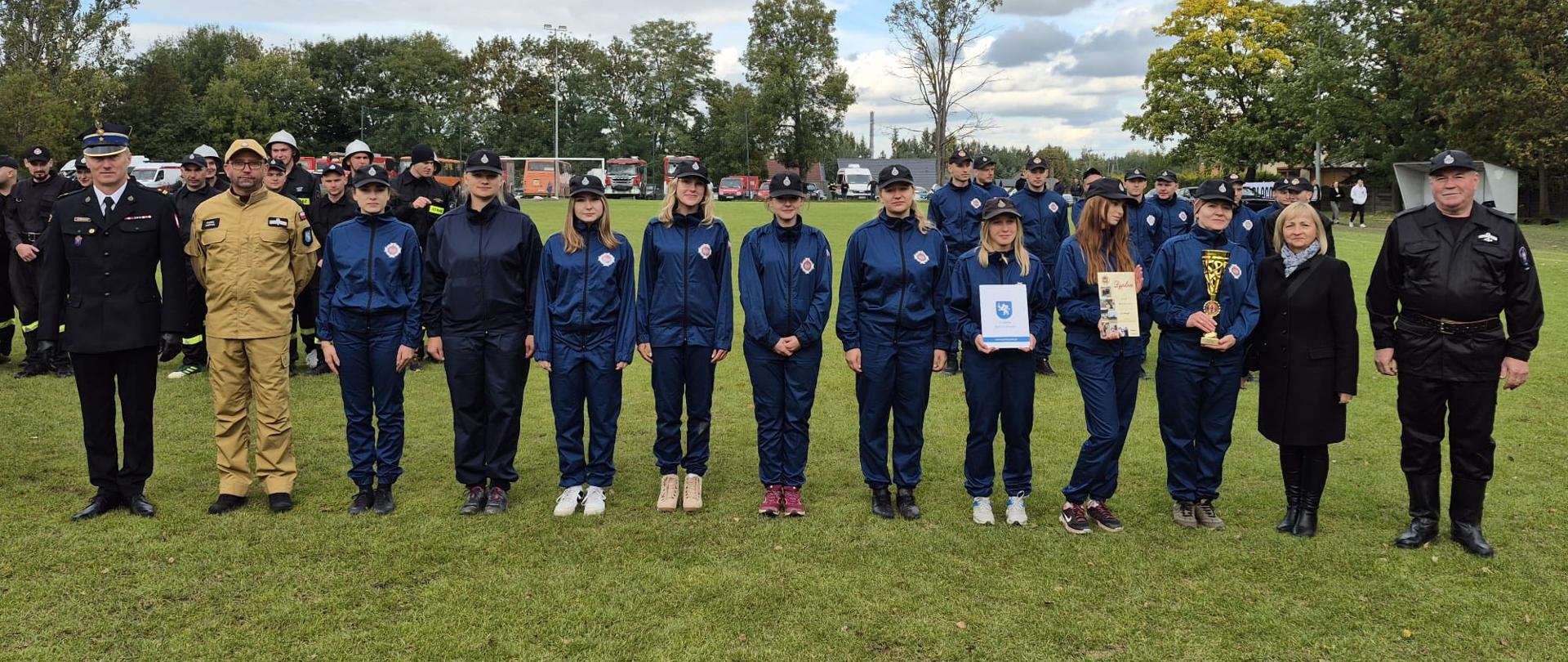 Zdjęcie obrazuje starostę, komendanta powiatowego PSP w Jędrzejowie oraz Prezesa Zarządu Oddziału Powiatowego OSP, którzy dekorują zwycięzców zawodów sportowo-pożarniczych.