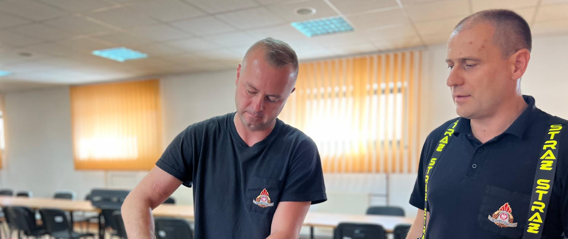 Na drugim zdjęciu strażak-ratownik u „fantoma - przekrój głowy do intubacji” wykonuje symulację przyrządowego udrożnienia dróg oddechowych. W pierwszej kolejności odchyla głowę do tyłu, następnie zakłada rurkę ustno-gardłową celem zabezpieczenia drożności dróg oddechowych.