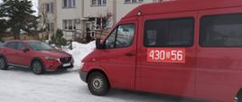 Przed budynkiem ośrodka zdrowia w Narwi na zaśnieżonej drodze stoi strażacki czerwony bus z numerami operacyjnymi 430 b 56.