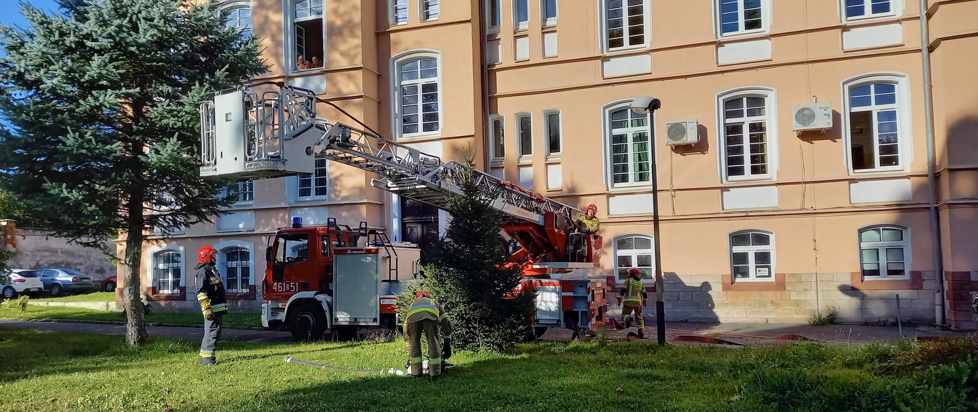 Widok na teren przy szpitalu. Strażacy ćwiczą ewakuację pacjentów szpitala.