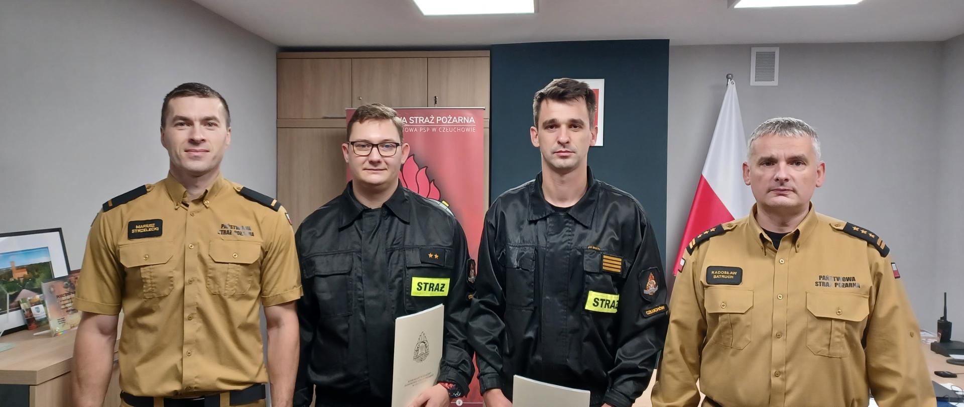 Komendant Powiatowy Państwowej Straży Pożarnej w Człuchowie st. bryg. Radosław Batruch stoi w gabinecie wraz z awansowanymi funkcjonariuszami.