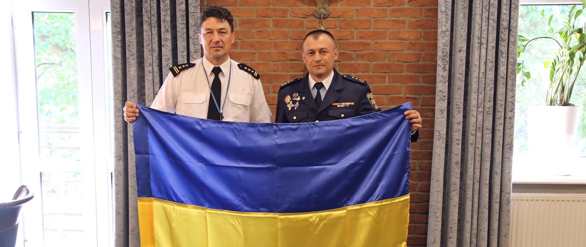 Na zdjęciu po lewej Komendant Centralnej Szkoły PSP, po jego lewej stronie płk. Rusłan Datsenko. Panowie wspólnie trzymają flagę Ukrainy