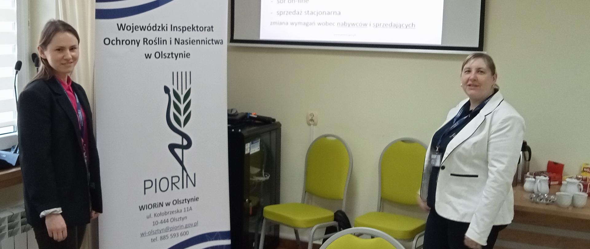 dwie osoby stoją przy rollupie PIORiN, na ścianie wyświetlany jest slajd