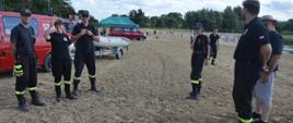 Piknik "Kręci mnie bezpieczeństwo nad wodą". Plaża na byłym poligonie wojskowym w Sierakowie. Druhowie z OSP w Rawiczu biorący udział w pikniku. W tle kąpielisko, drzewa, namiot, samochody pożarnicze oraz ponton.