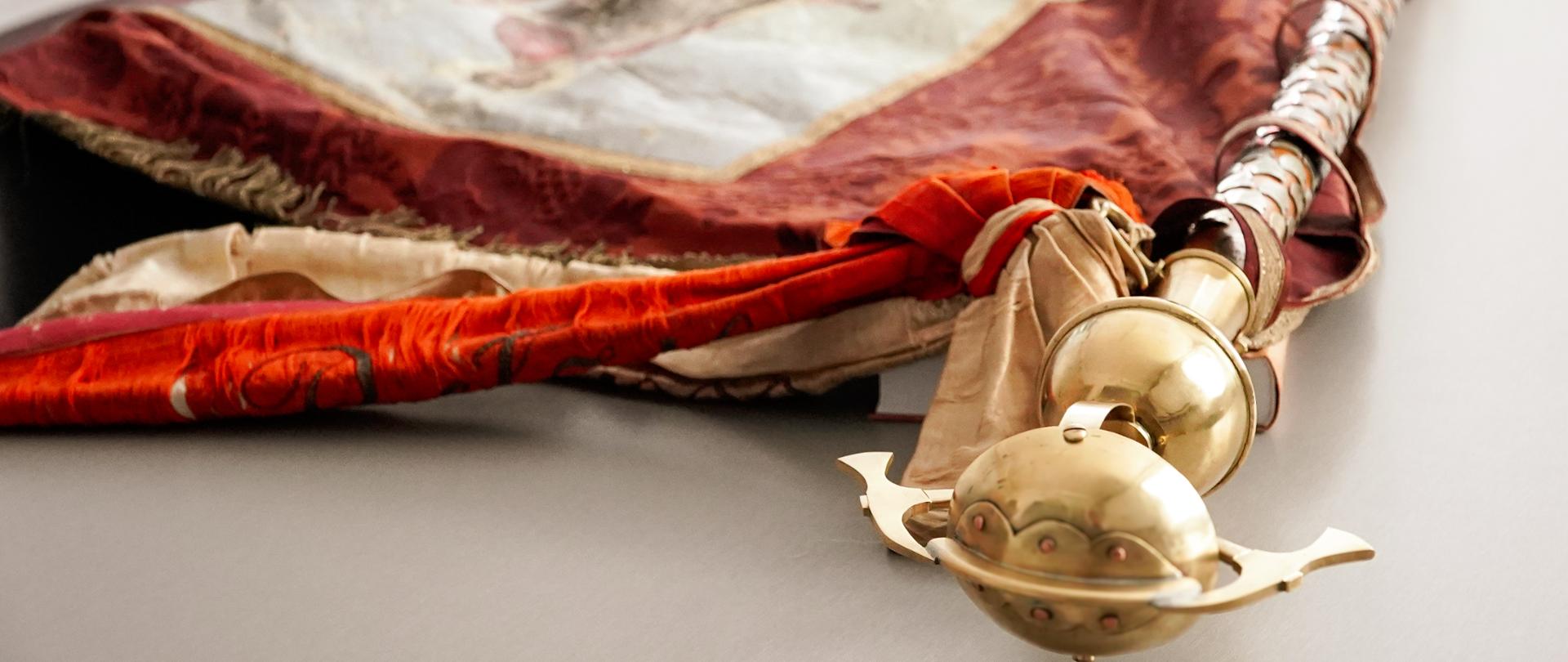 Historyczny sztandar Ochotniczej Straży Pożarnej z Bełza z odtworzoną głowicą drzewca, datowany na lata 1882–1929.