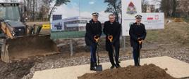 Wielkopolski komendant wojewódzki , wojewoda wielkopolski i komendant główny PSP wbijają szpadle w ziemię, za nimi wizualizacja rozpoczętej inwestycji
