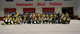 Przed budynkiem komendy, na tle bram garazowych do wspólnego zdjęcia pozują uczestnicy szkolenia wraz z funkcjonariuszami PSP. 