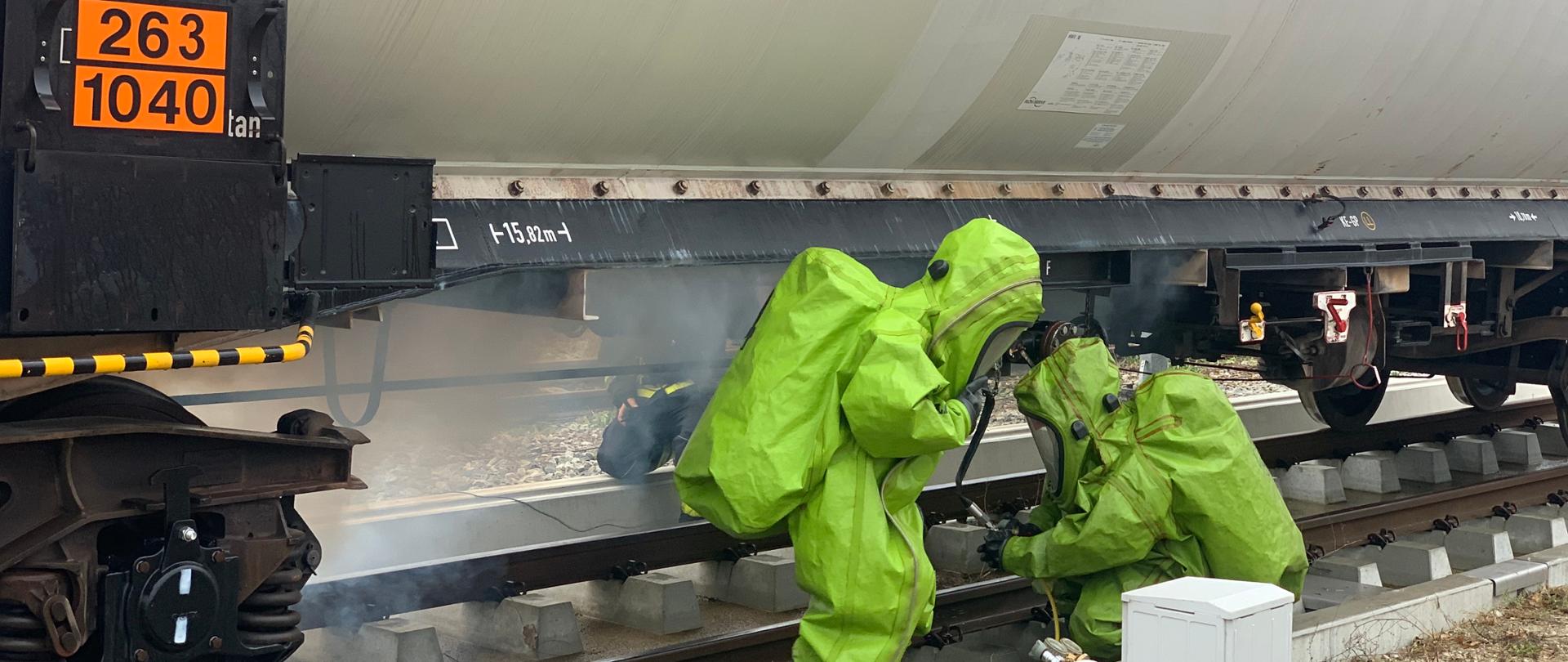 Dwóch strażaków ubranych w ubranie gazoszczelne próbuje zatamować wyciek substancji z cysterny kolejowej. Ćwiczenia PATROL-21