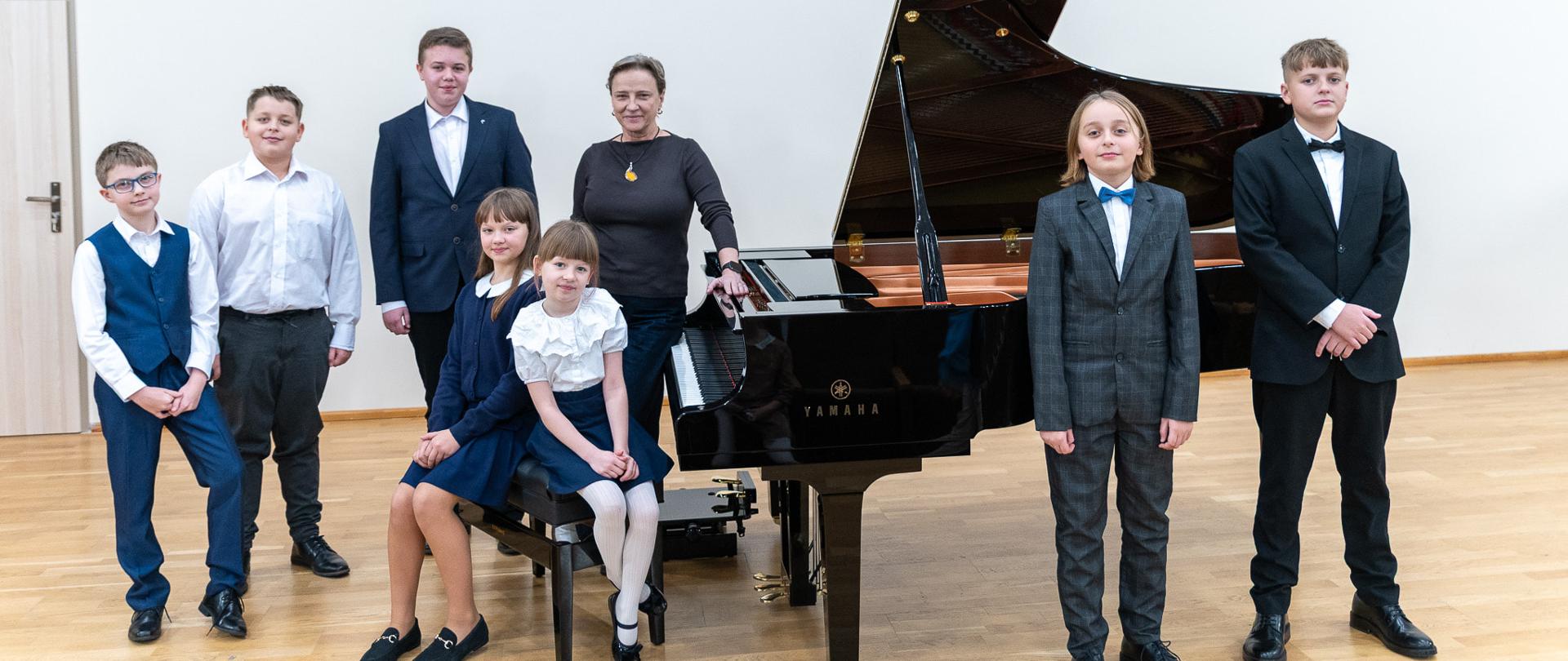 Przy fortepianie pozują do zdjęcia uczniowie z klasy fortepianu wraz z nauczycielką Elżbietą Lieder. 