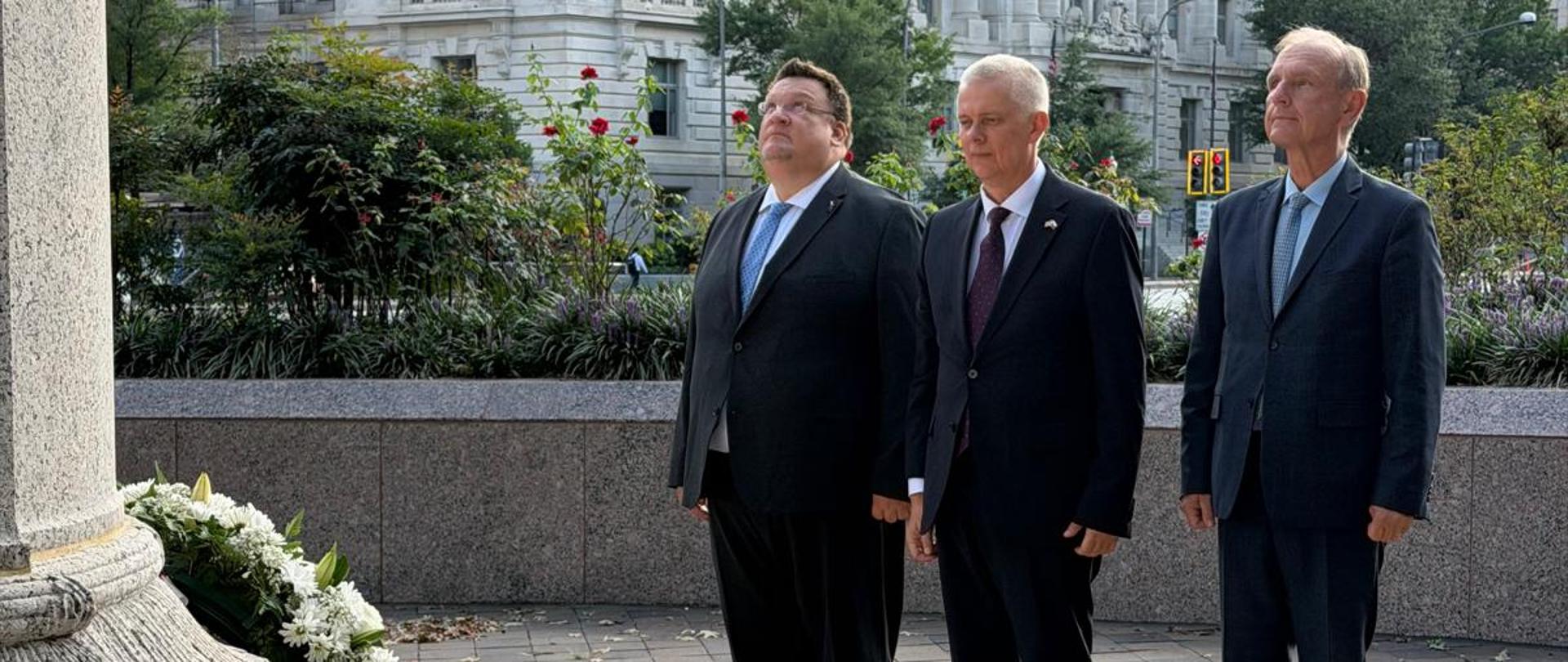 Na zdjęciu minister Tomasz Siemoniak (w środku), Bogdan Klich (po prawej) oraz płk Paweł Szota (po lewej) stoją przed pomnikiem generała Kazimierza Pułaskiego w Waszyngtonie. Po lewej stronie zdjęcia widać pomnik i wieniec (białe kwiaty). W tle zdjęcia budynki i zieleń.
