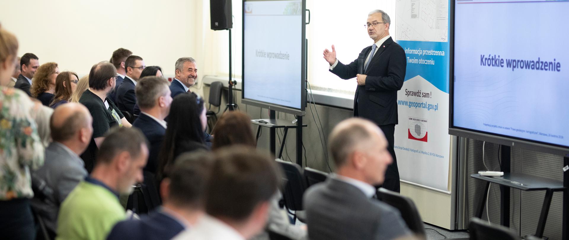 przed siedzącymi uczestnikami konsultacji z mikrofonem stoi minister Jerzy Kwieciński