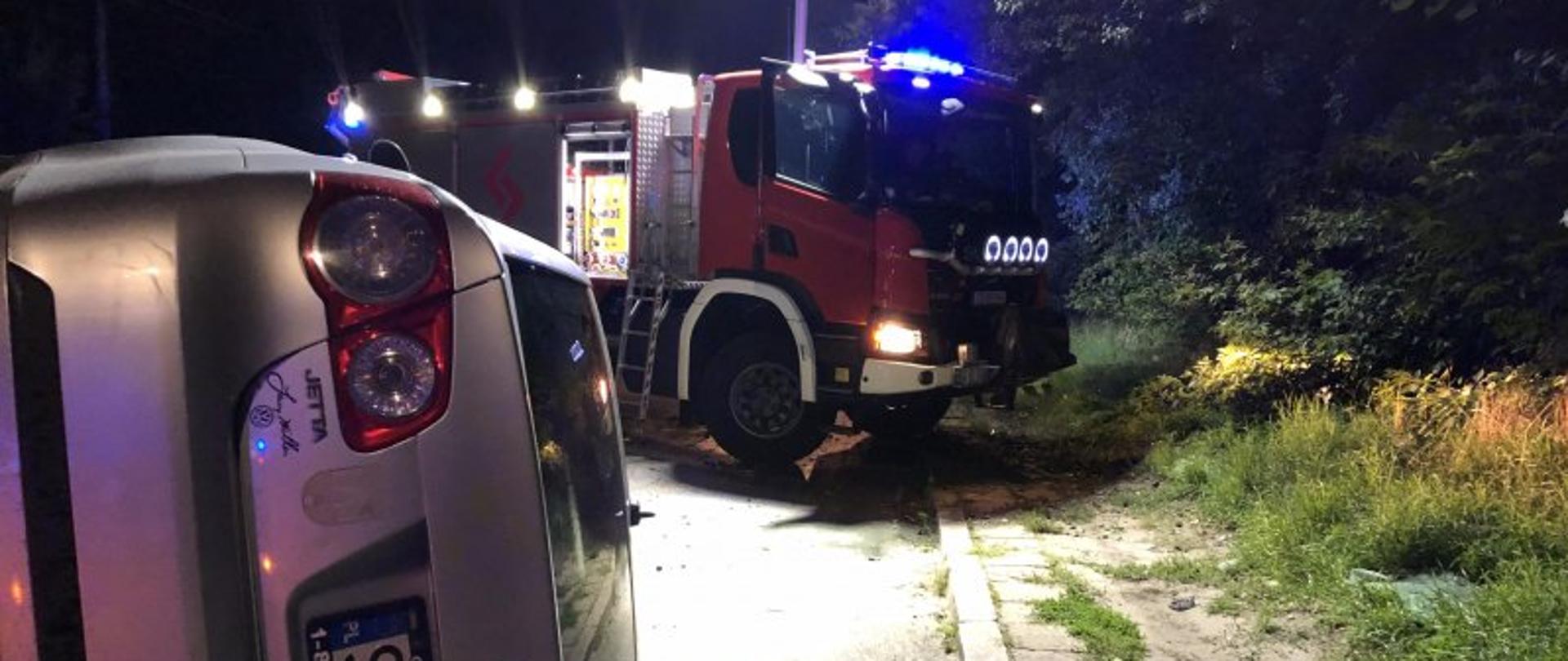  Częstochowa - wypadek - uszkodozny samochód osobowy przewrócony na bok, w tle samochód pożarniczy, widok od tyłu samochodu osobowego