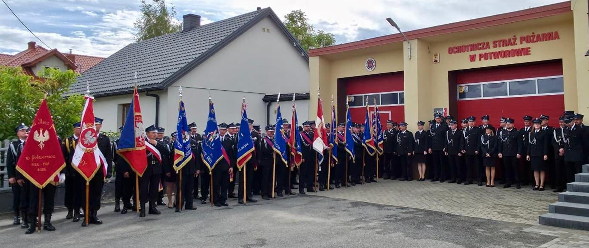 Poczty sztandarowe oraz strażacy zgromadzeni przed strażnicą OSP Potworów podczas uroczystości jubileuszowych związanych ze 100-leciem jednostki.