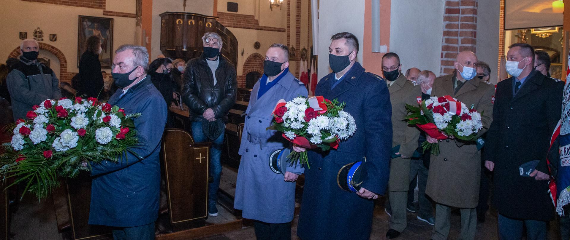 Uczestnicy uroczystości stoją w kolejce do złożenia kwiatów.
