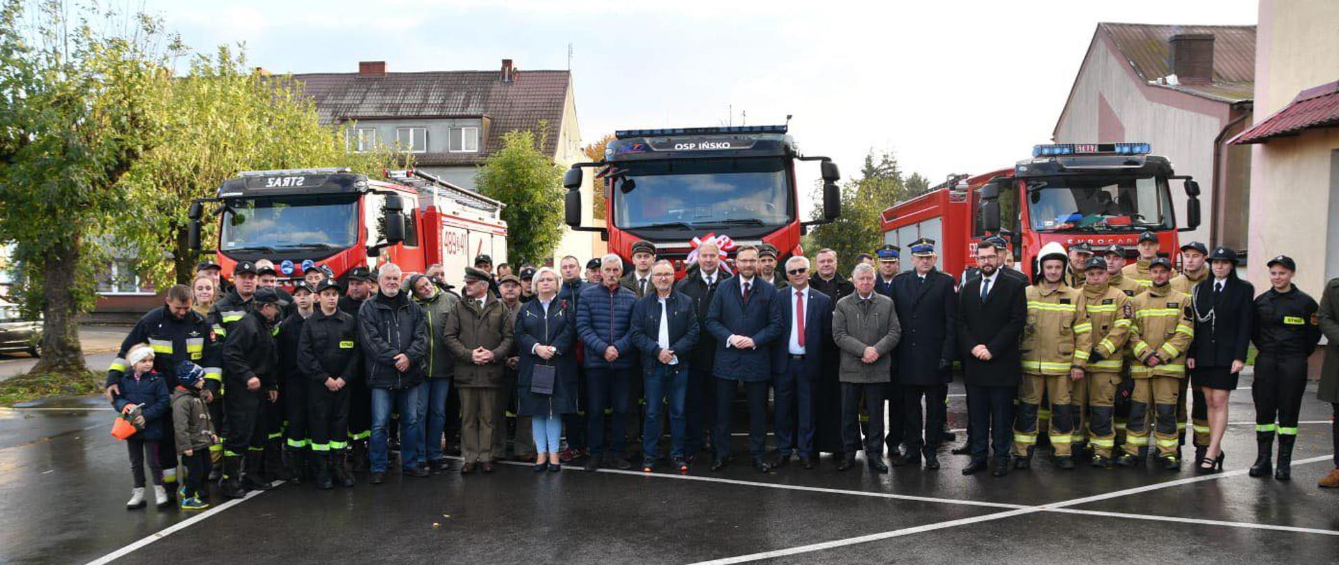 Zdjęcie grupowe uczestników ceremonii przekazania samochodu. W tle park maszynowy OSP Ińsko.