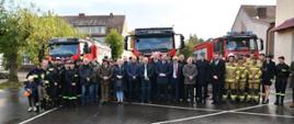 Zdjęcie grupowe uczestników ceremonii przekazania samochodu. W tle park maszynowy OSP Ińsko.