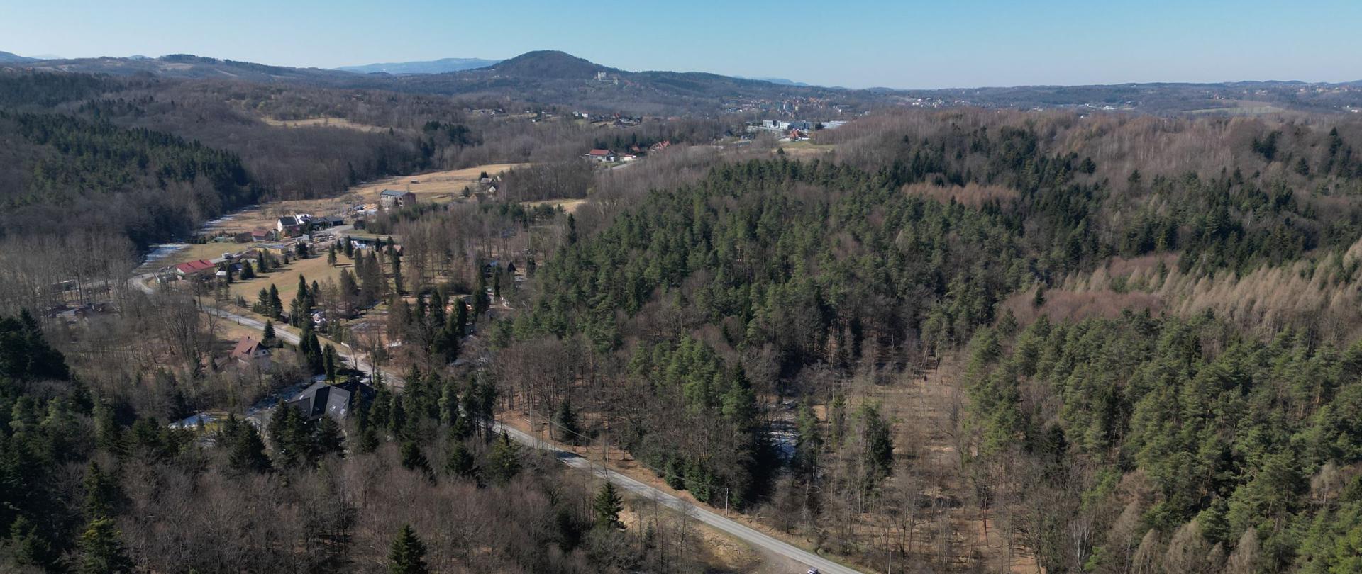 zdjęcie lotnicze terenu przyszłego węzła Kalwaria Wschód, teren zalesiony, pofałdowany, w oddali zabudowania, w tle wzgórza