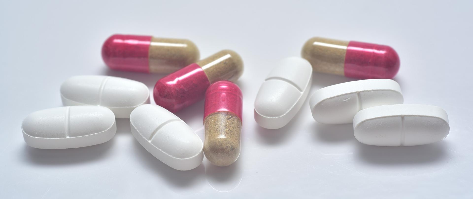 kilka białych i różowych tabletek leżących na białym blacie.