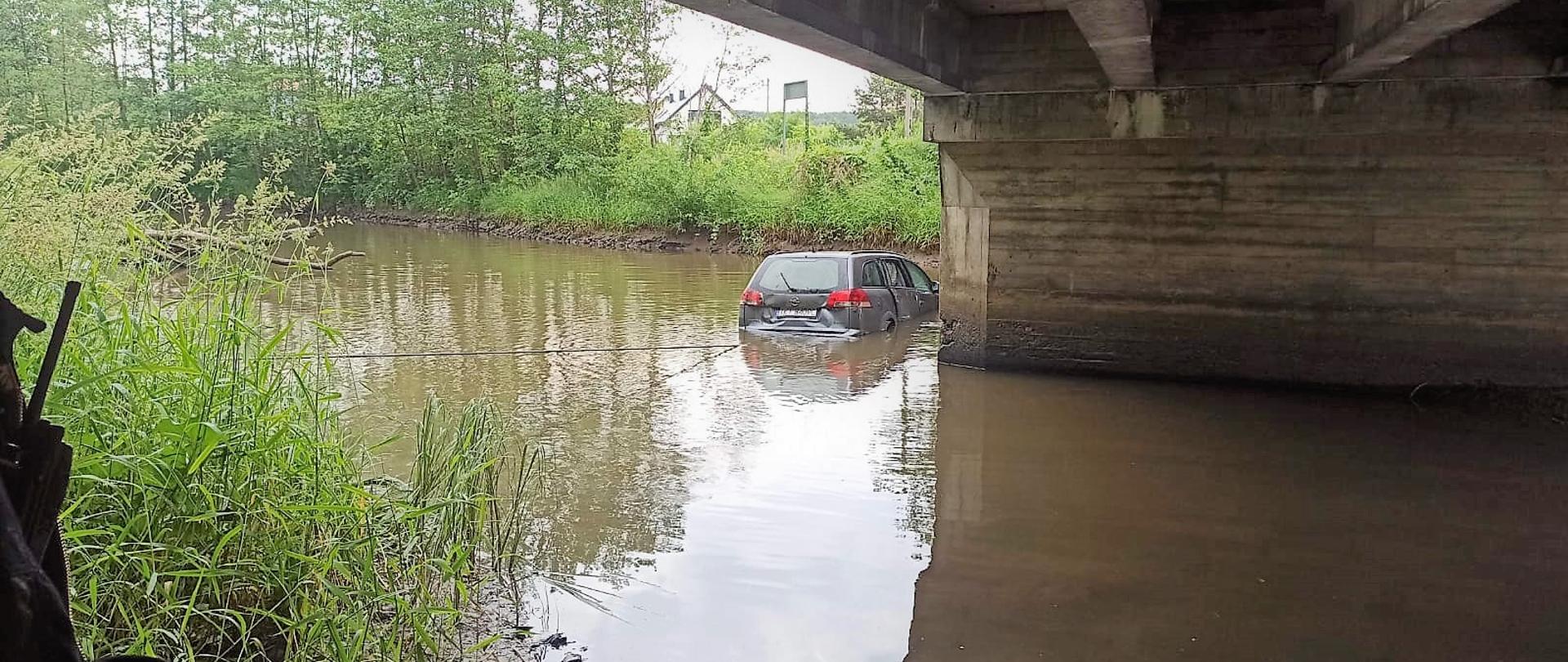 Na zdjęciu przepływająca pod mostem rzeka Lubrzanka, w której znajduje się samochód osobowy.