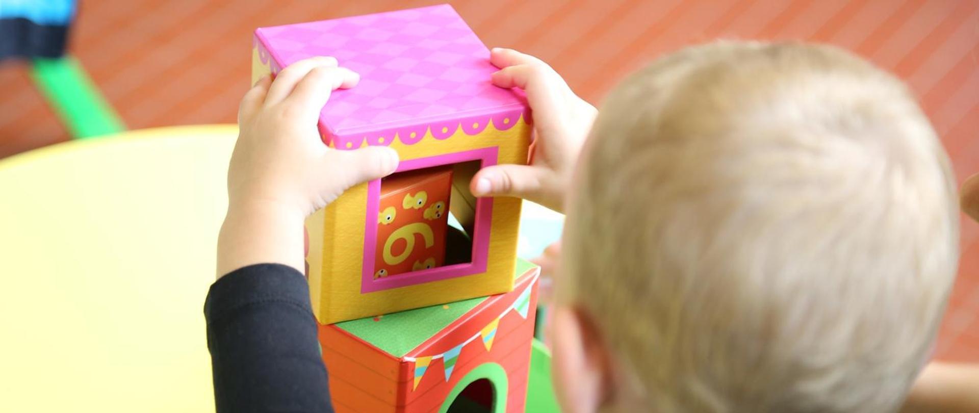 Na zdjęciu znajduje się głowa dziecka, które bawi się kolorowymi zabawkami