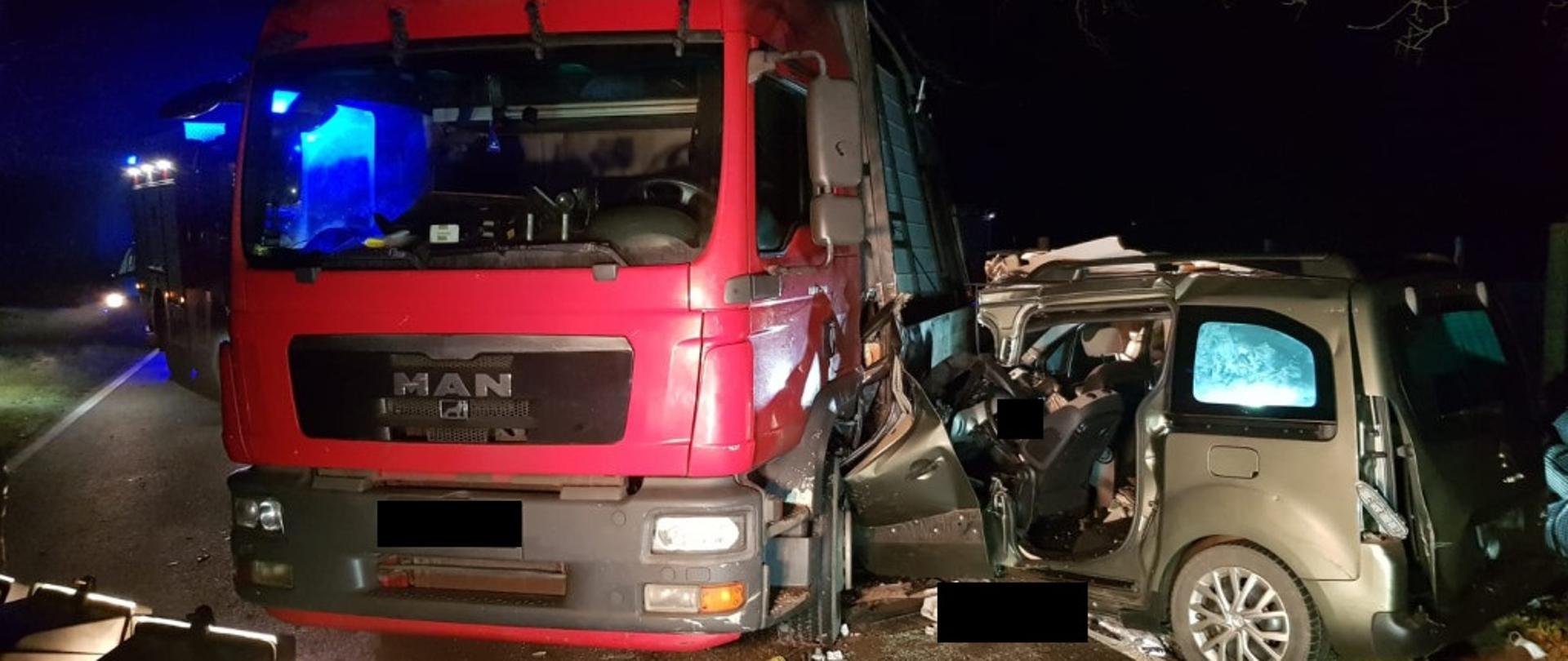 Widać czerwony samochód ciężarowy, w lewy bok uderzył pojazd osobowy, który jest mocno uszkodzony